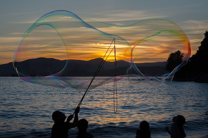 silhouette of man making large bubbles during sunset