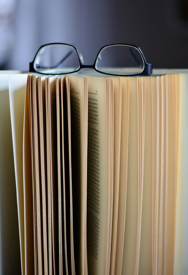 selective focus photography of opened book with eyeglasses on top of it
