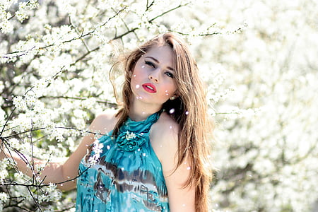 fashion photography of woman posing and wearing blue and black halter sleeveless top standing beside white flowering plants