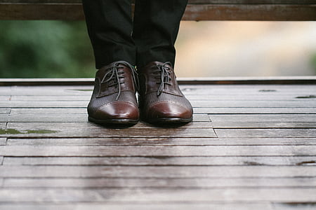 person wearing brown leather shoes standing on brown surface