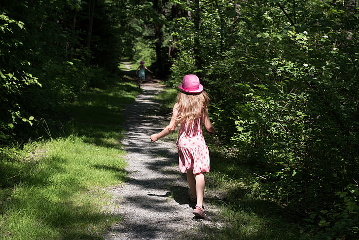 girl wearing pink hat running through forest