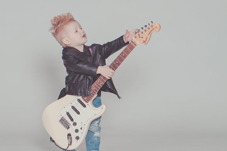 boy in black leather jacket holding white electric guitar