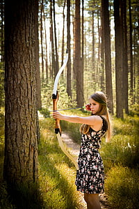 woman in black floral mini dress holding long bow standing beside tree