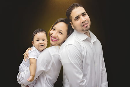 woman and man in white dress shirts leaning each other while holding a baby