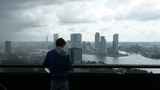 man wearing blue shirt holding hand rail viewing high rise building