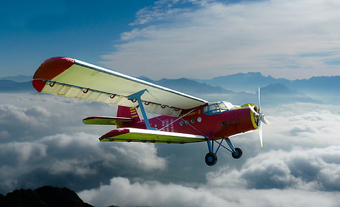 red and white biplane flying over sea of clouds