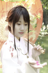woman wearing white kimono holding oil paper umbrella and pink petaled flower