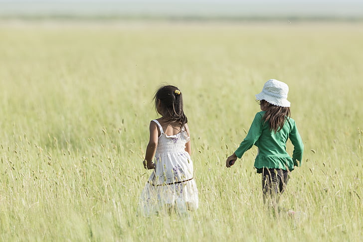 two girls walking on grass field during daytime