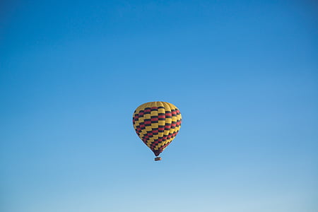 yellow, red, and black hot air balloon flying under blue sky