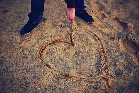 person drawing heart on sand
