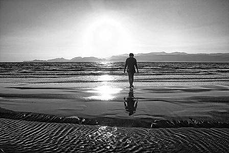 grayscale photo of person walking towards sea