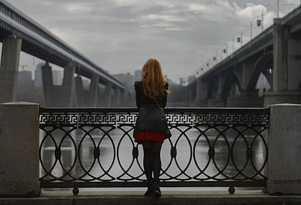 woman wearing black jacket standing beside black metal rails watching concrete bridge