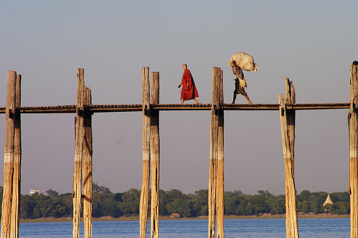 man in red robe standing on wooden bridge