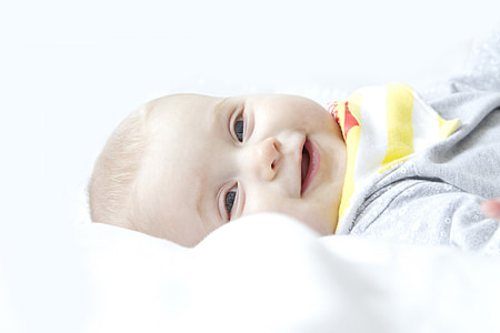 smiling baby lying on white textile