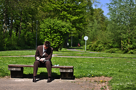 man wearing black suit jacket sitting on brown concrete bench