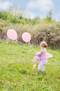 toddler wearing pink sleeveless top holding balloons standing on grass field