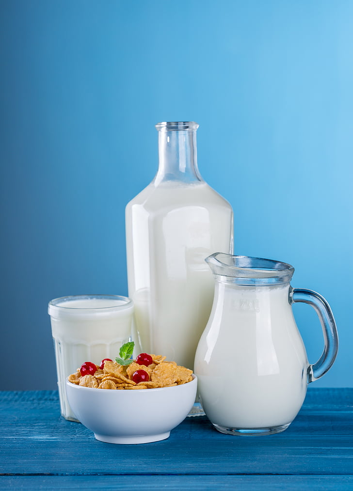 milk in clear glass pitcher, bottle and drinking glass and cereals on white ceramic bowl