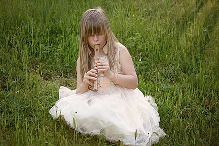 girl wearing white dress sitting on grass while playing brown flute
