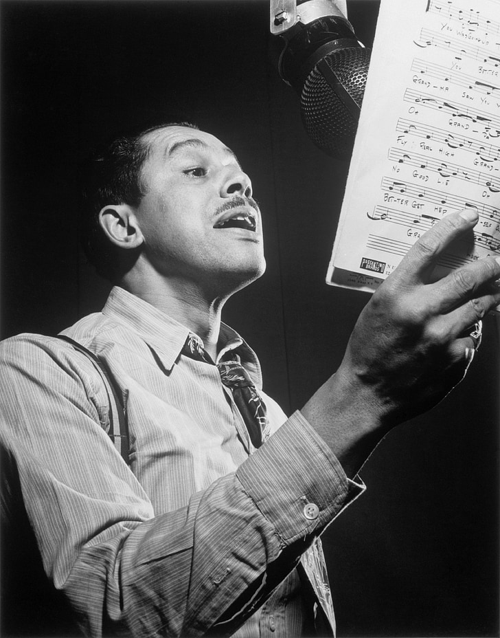 graysale photography of man singing while holding musical script