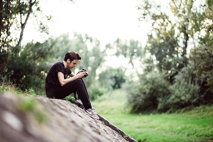 man browsing camera while sitting on the cliff