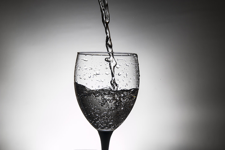 pouring water on wine glass grayscale photography