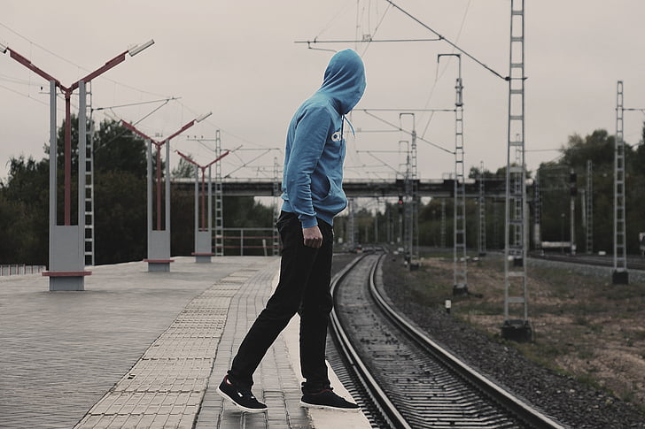 man wearing blue pullover hoodie walking on railroad photography during daytime