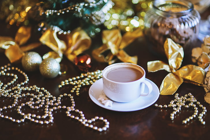 cup of coffee on white ceramic saucer beside silver-colored beads, gold ribbons, and silver baubles Christmas ornaments