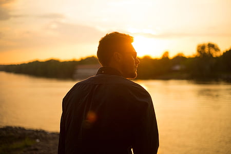 man wearing sunglasses in front of calm body of water during golden hour