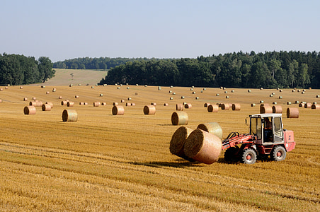 red tractor with hay stacks on brown field during daytime