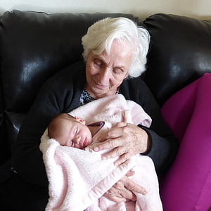 grandmother in black long-sleeved top sits while holding baby