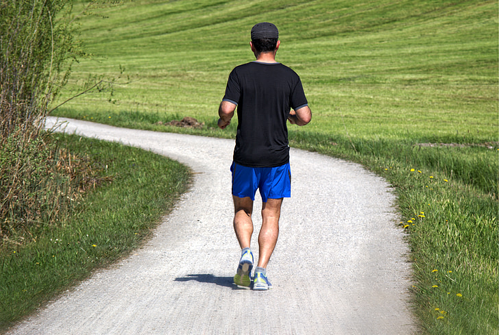 man jogging on gray pathway between grass fields photo