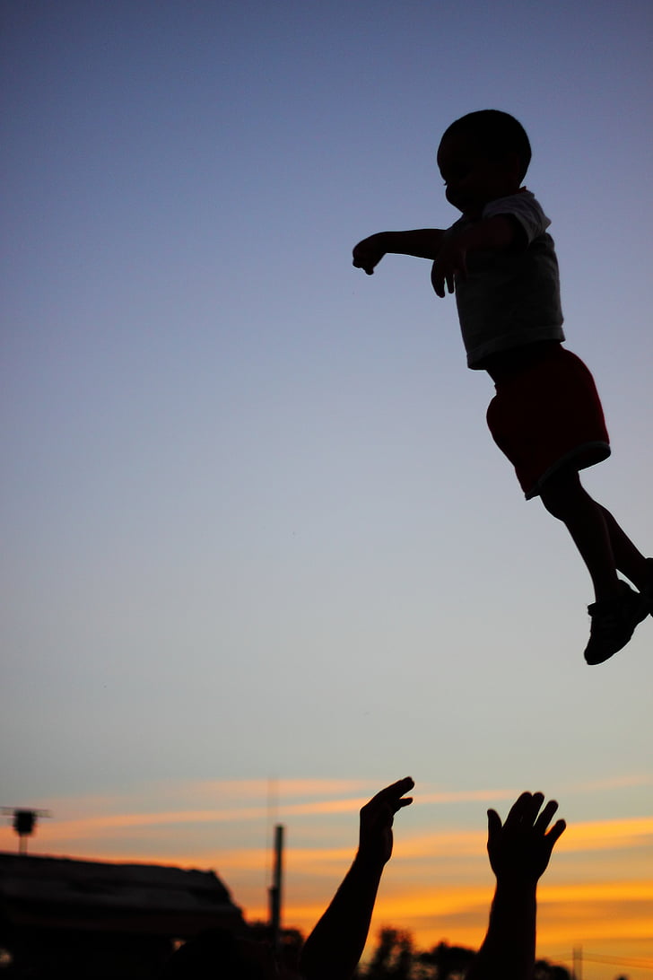 silhouette photography of child on air with a person catching him