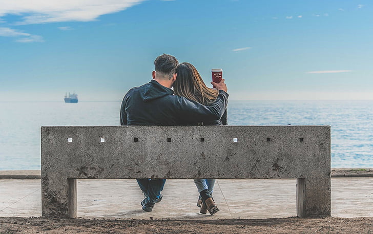 man and woman sitting on bench beside sea