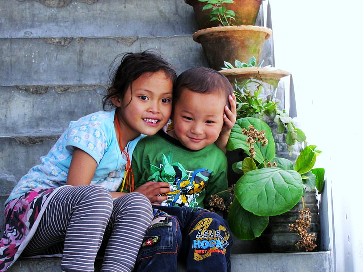 smiling girl and boy sitting on staircase beside plants during daytime