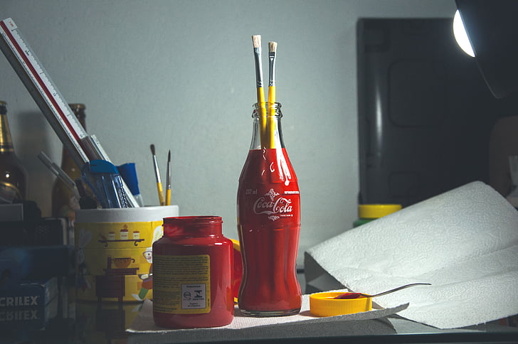 red Coca-Cola glass bottle with two paintbrushes