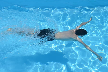photo of man wearing black shorts swimming in pool