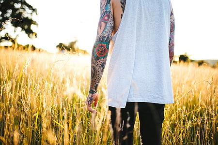 person wearing white shirt with multicolored tattoo walking on green grass field during daytime