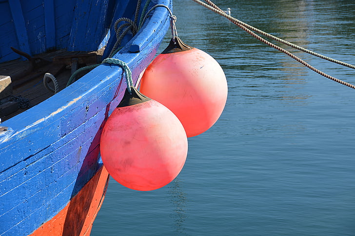 Fishing tackle on the pier. Moored fishing boat, red bright fishnet, ropes,  lifebuoys. Pier with a red fishing net in the foreground. Colorful marine  picture against a bright blue sky. Stock Photo