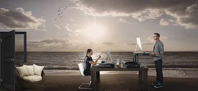 man and woman facing computer monitors on top of beach