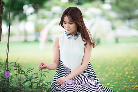 black haired woman wearing white and black striped sleeveless dress sitting on green grass field
