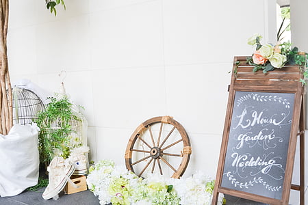 brown sandwich board beside carriage wheel and white flowers