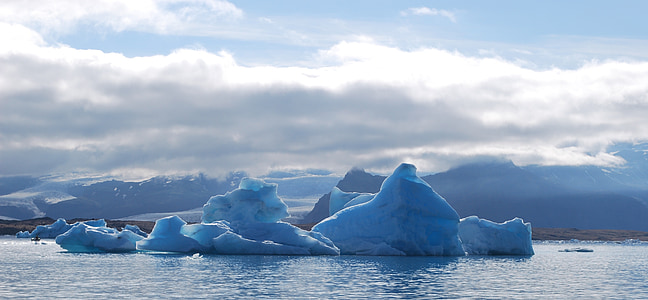 ice bergs floating on sea under cloudy blue sky