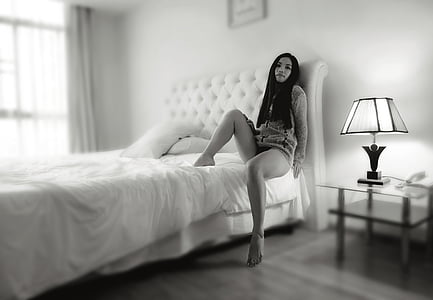 woman wearing mini dress sitting on bed near table lamp