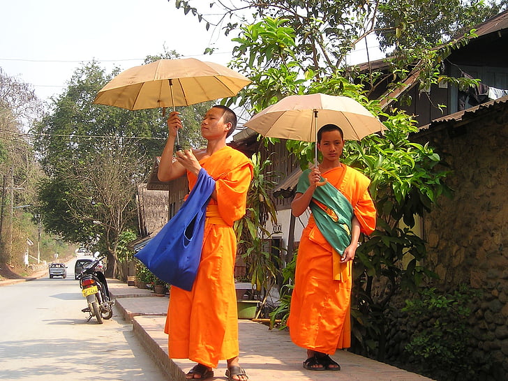 two monks with umbrellas at the sidewalk near house during day