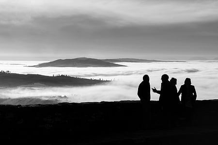 silhouette photography of four person standing far away from mountains covered on clouds