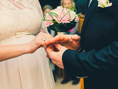 woman wearing white wedding dress and man wearing black suit holding a ring