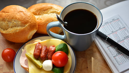 two baked breads beside ceramic cup filled with black liquid, bread knife and salad