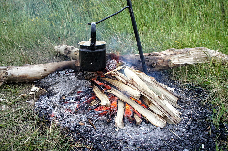 cooking pot on metal rod near wood log