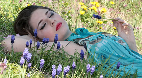 woman lying on grass holding purple grape hyacinth flower during daytime