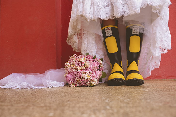 person wearing black-and-yellow rain boots beside flower bouquet
